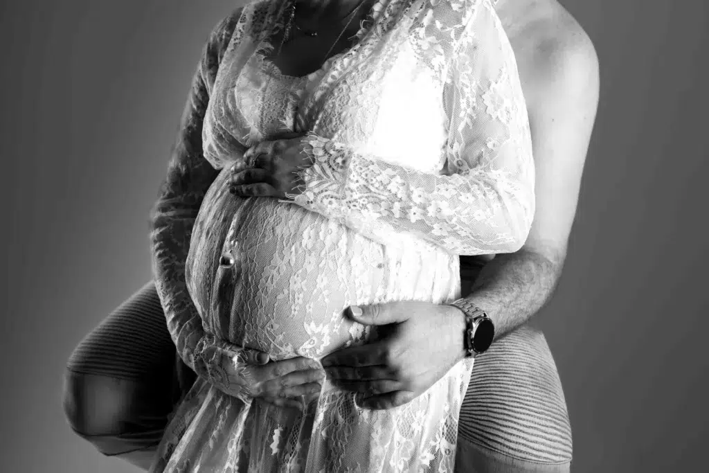 Femme enceinte en robe de dentelle lors d'une séance photo maternité en noir et blanc