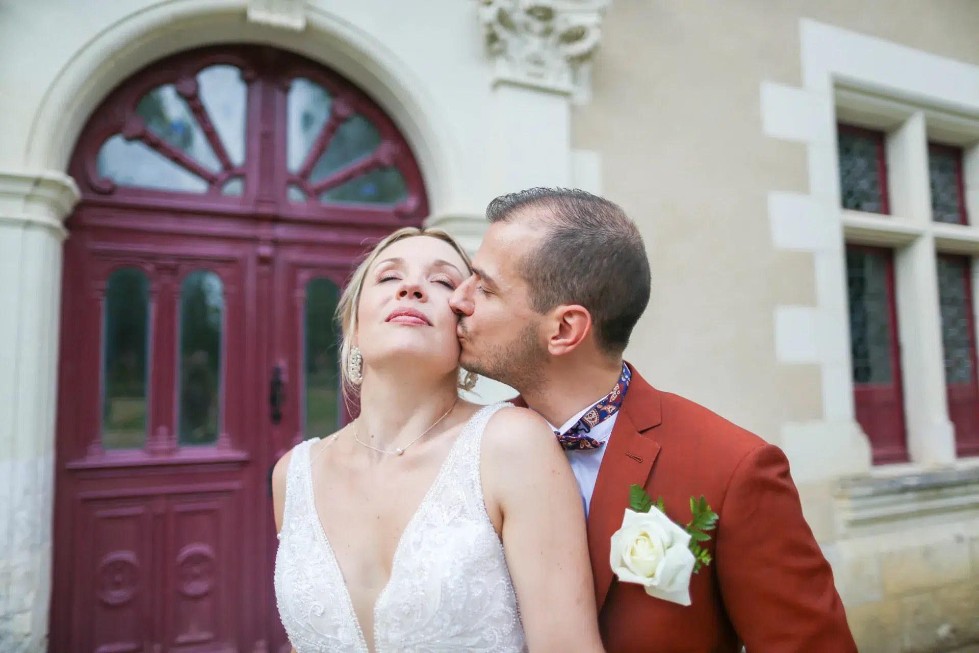 Couple de mariés enlacés devant une porte rouge lors de leur séance photo de mariage